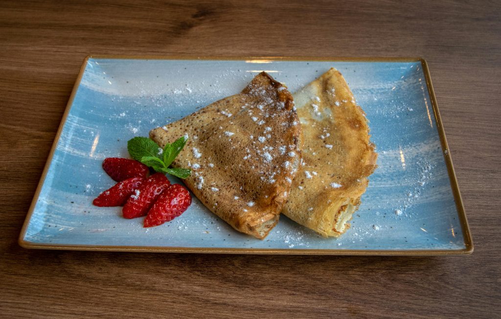 A plate of crêpes dusted with powdered sugar, served with strawberries and mint.