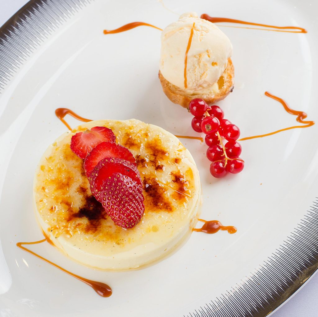 Gourmet crème brûlée topped with fresh strawberries and red currants on a fancy plate.